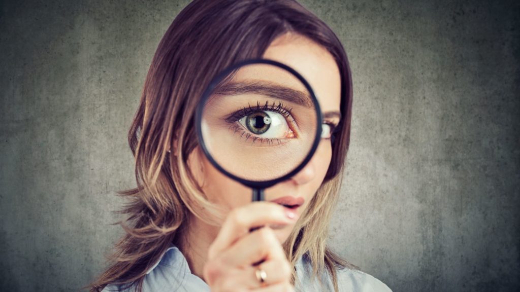 Woman peering through a magnifying glass, illustrating questions about company culture