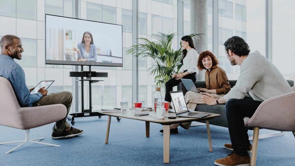 Hybrid meeting with colleagues in a room and one joining by video, illustrating new ways of working