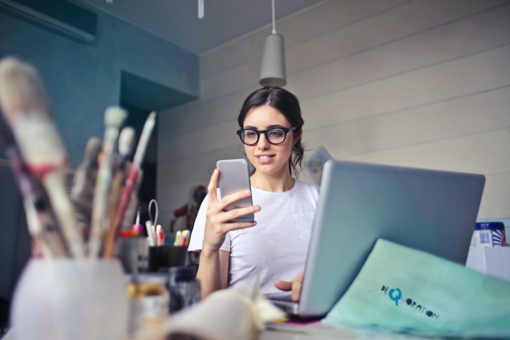 Employee checking her phone beside a laptop, illustrating action to retain and engage staff