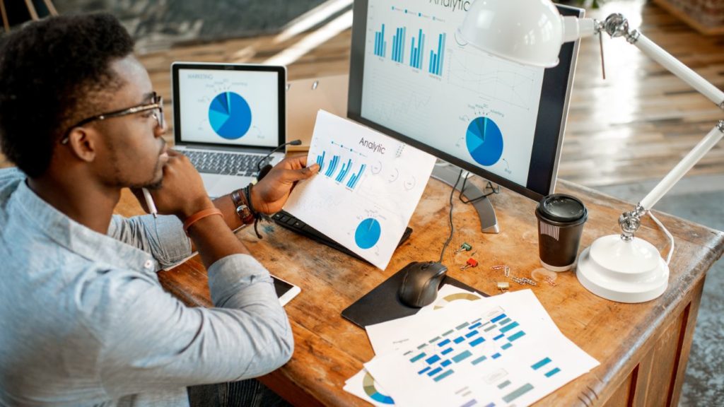 Employee studying analytics charts on screen and paper, illustrating people analytics in use