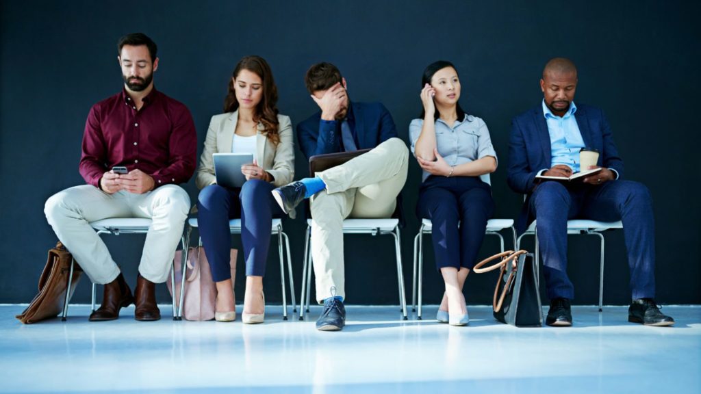 Candidates waiting in a row of chairs for job interviews, illustrating a busy hiring market