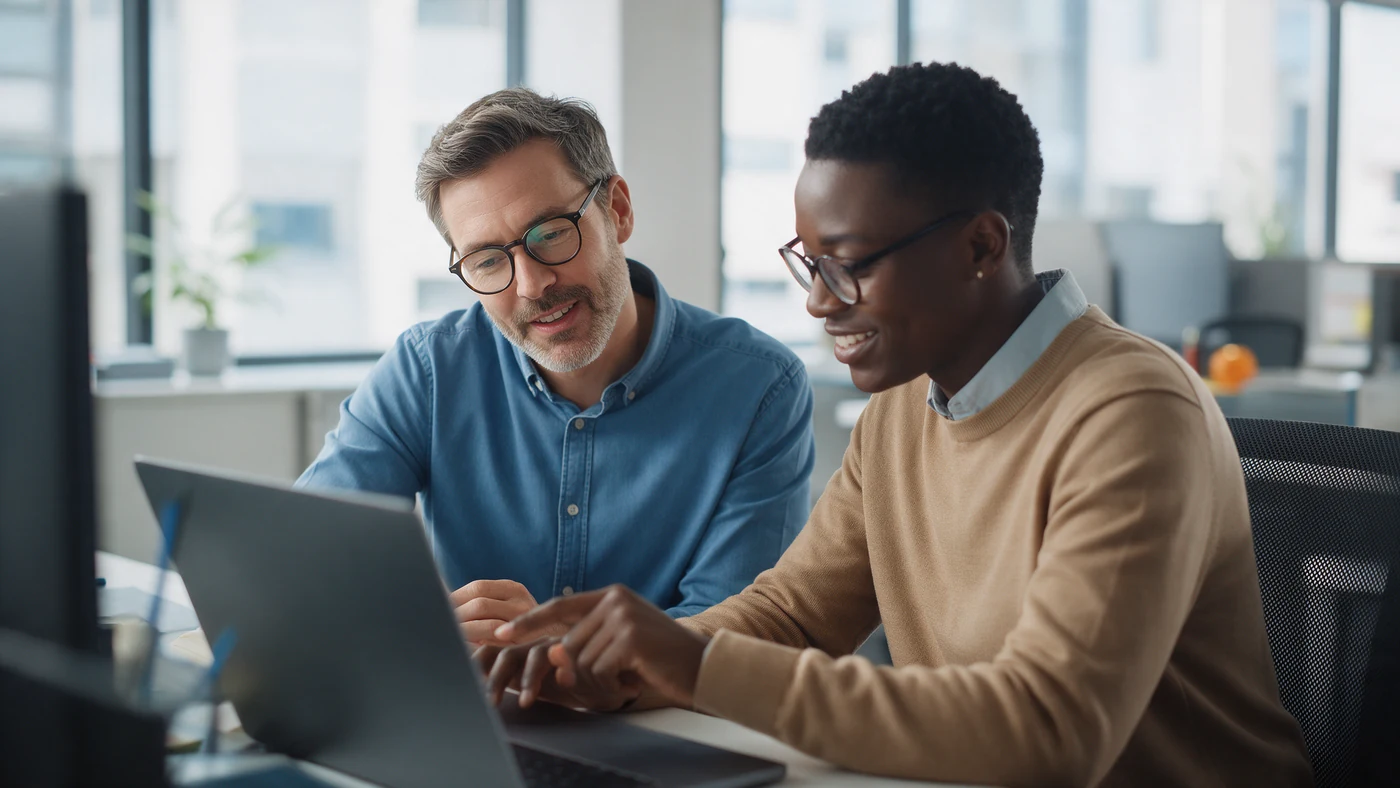 A manager and an employee review a personal development plan together on a laptop during a one-to-one